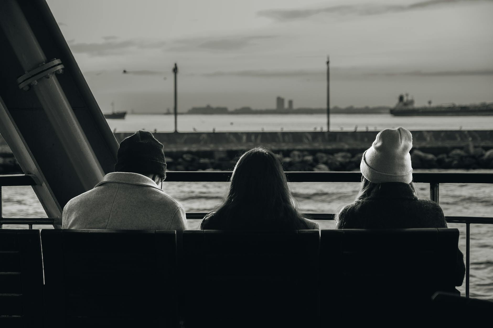 Three people sitting on a bench, gazing at the tranquil waterfront in a serene monochrome setting.