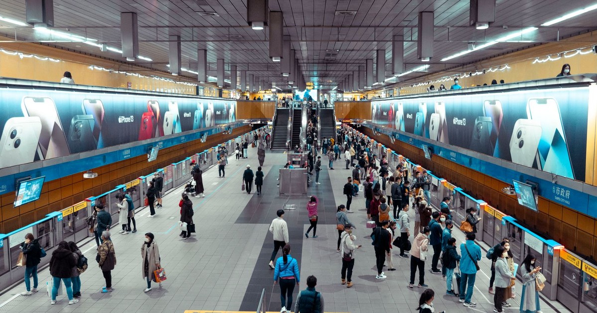 A bustling underground train station with people waiting and walking near escalators.