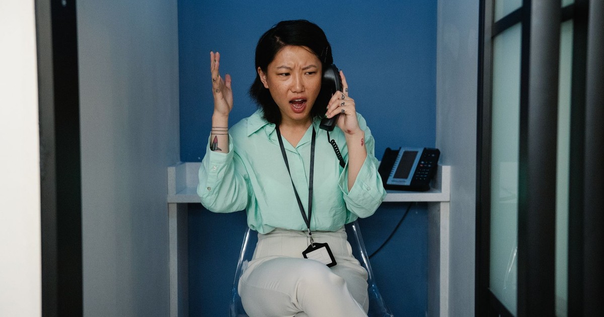 An east Asian woman expressing frustration during a phone call at the workplace.