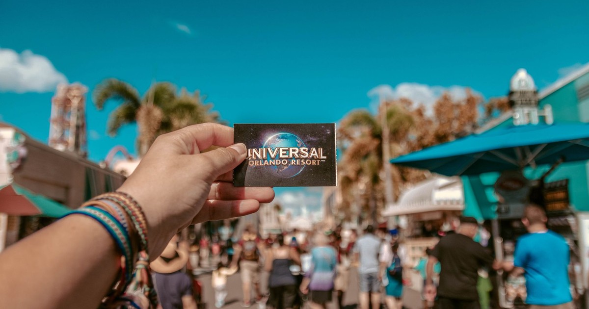A hand holding a Universal Orlando Resort ticket in a bustling theme park setting.