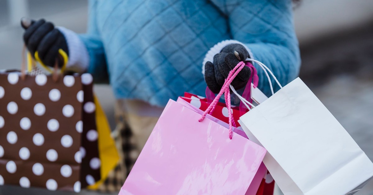 Crop anonymous female in blue soft sweater with many different colorful gift bags on blurred background