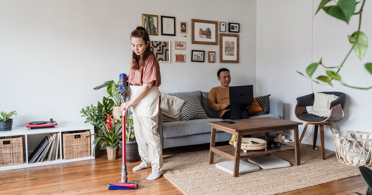 Woman vacuuming while man works remotely on laptop in cozy living room.