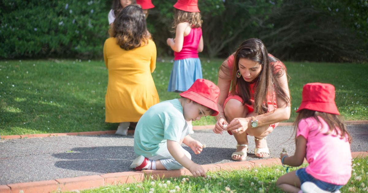 A group of children and caregivers wearing red hats exploring a garden.