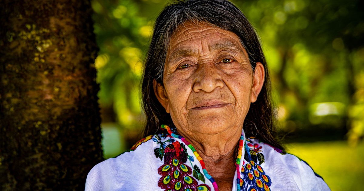 Elderly indigenous woman in colorful traditional attire, outdoors, close-up.