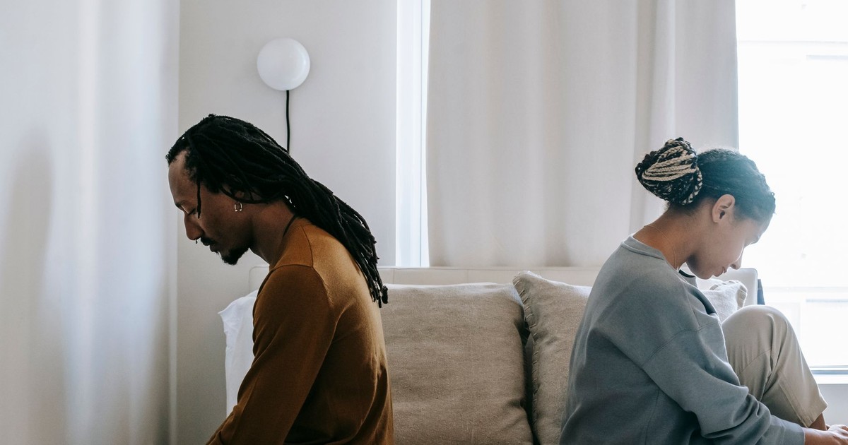 Side view unhappy sorrowful African American couple sitting on bed back to back after having argument