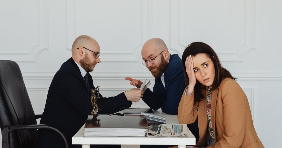Two lawyers discuss documents with a worried client in a professional office setting.