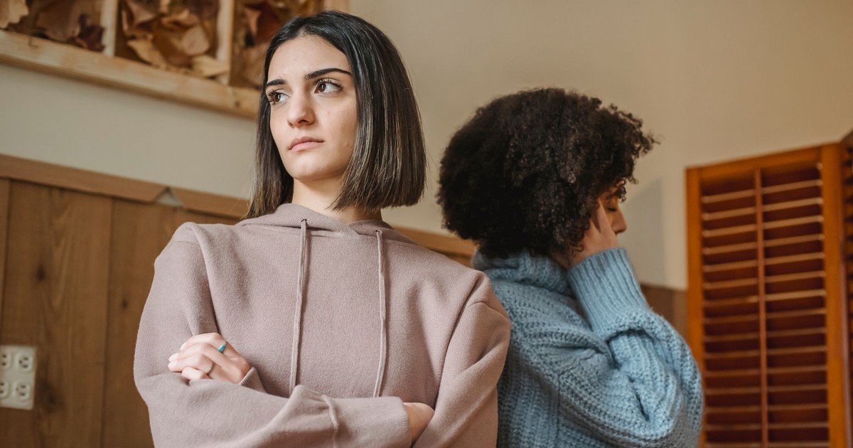 From below of unsatisfied multiracial women in casual clothes with crossed arms standing in light room during quarrel at home