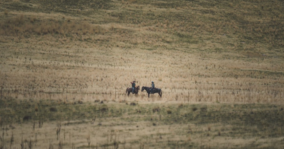 Two cowboys ride horses across a vast, scenic landscape in Utah, USA.