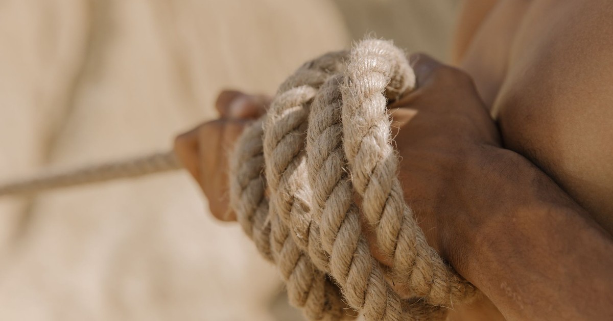 A close-up view of a person's hands tightly gripping a rope during a tug-of-war competition outdoors.
