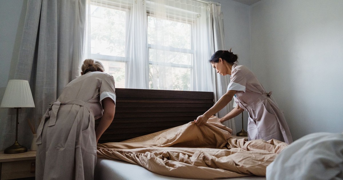 Two housekeepers making a bed in a sunlit bedroom, showcasing cleanliness and attention to detail.
