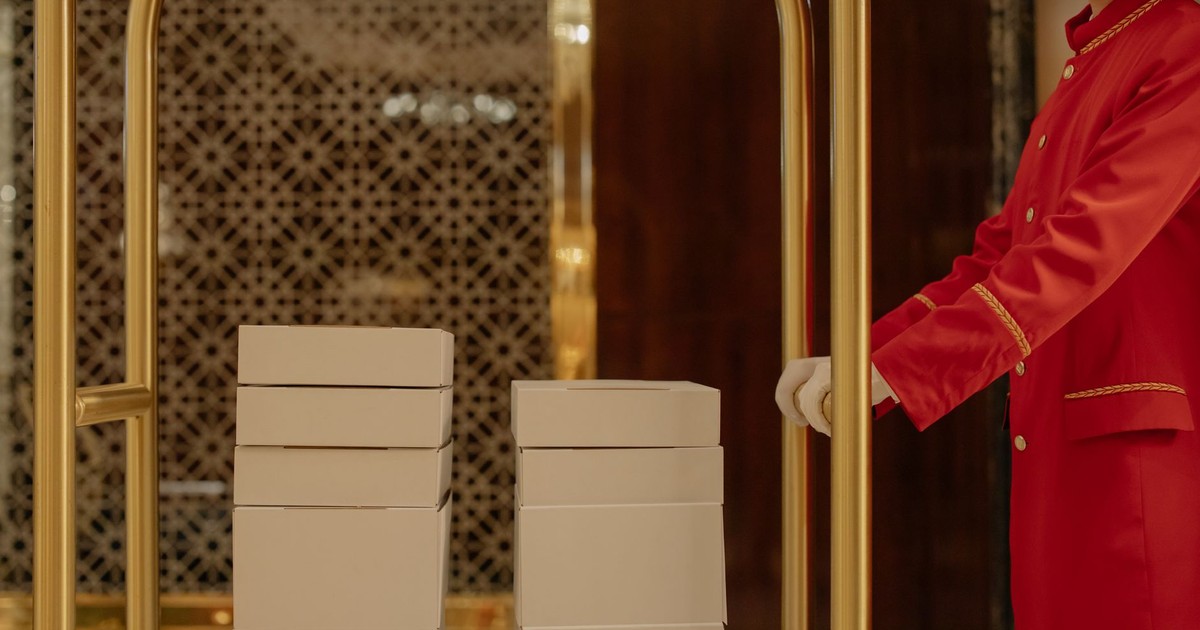 Hotel porter in red uniform assisting with luggage cart in a luxury hotel setting.