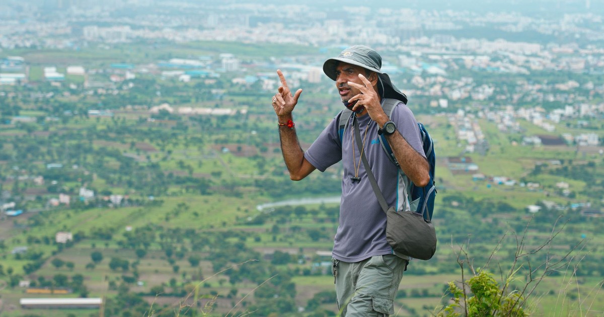 Man on a hike with a beautiful view of Pune city in the background, showcasing adventure and nature.