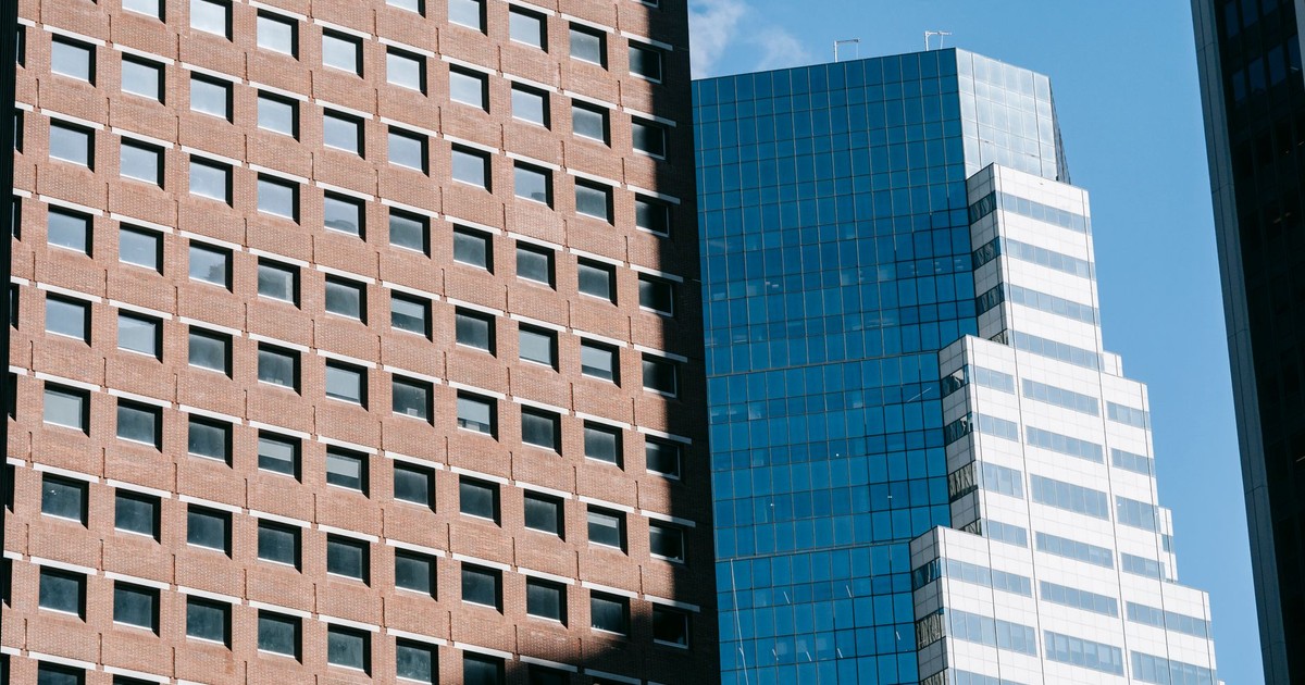From below of multistory residential building located near modern skyscraper in megapolis under blue sky