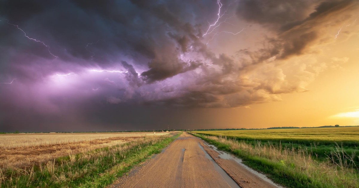 Stunning photo of a thunderstorm with lightning over a wheat field and dirt road in Oklahoma.
