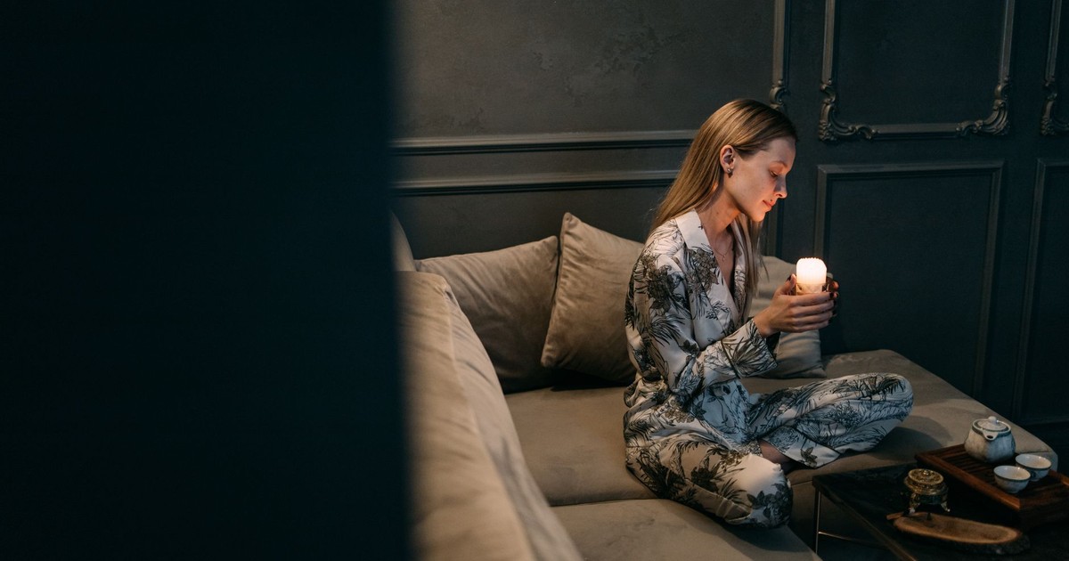 Woman in pajamas holding a candle, sitting on a cozy couch in a serene room.