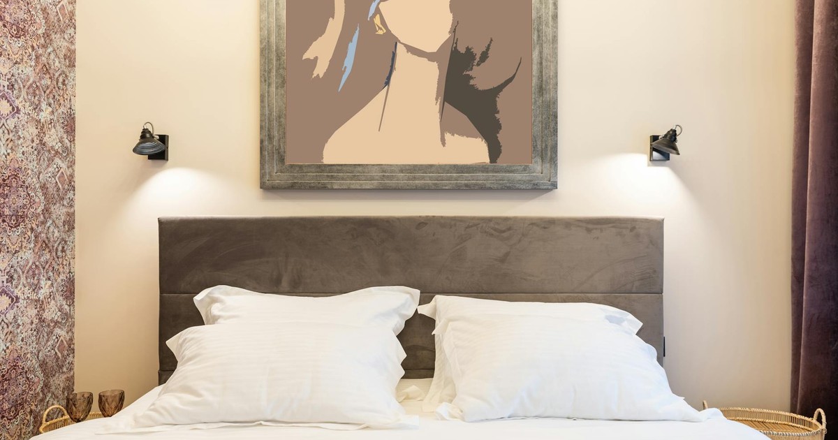 Soft pillows on bed against artwork on wall with shiny lamps and ornament in house