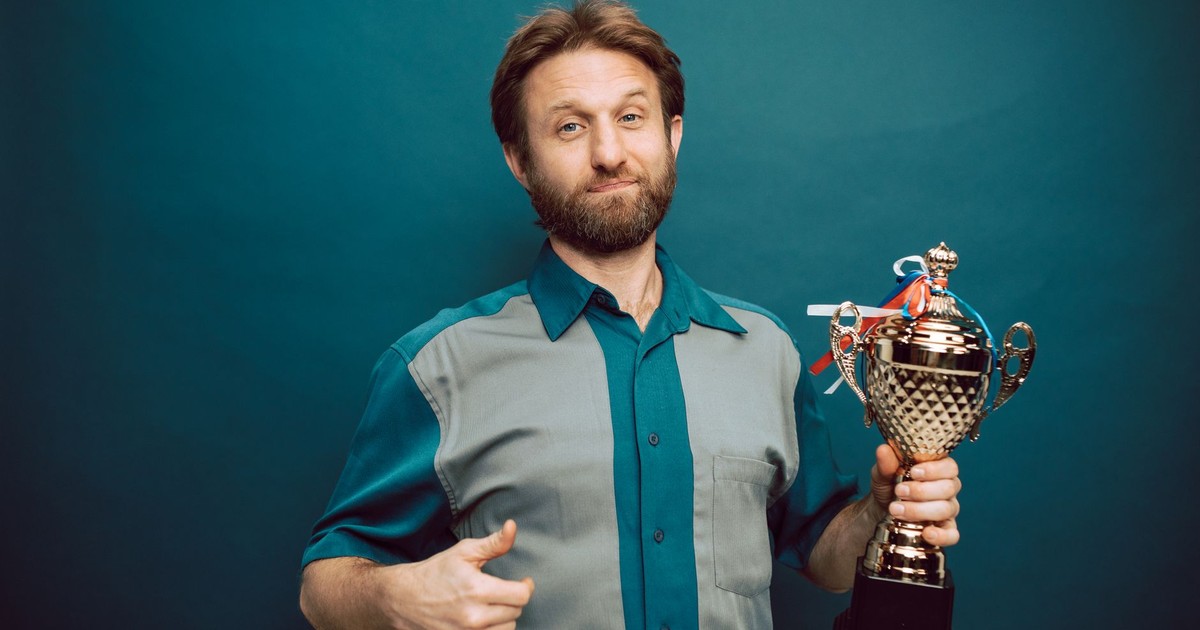 Confident man posing in studio holding a shiny trophy, showing pride in accomplishment.