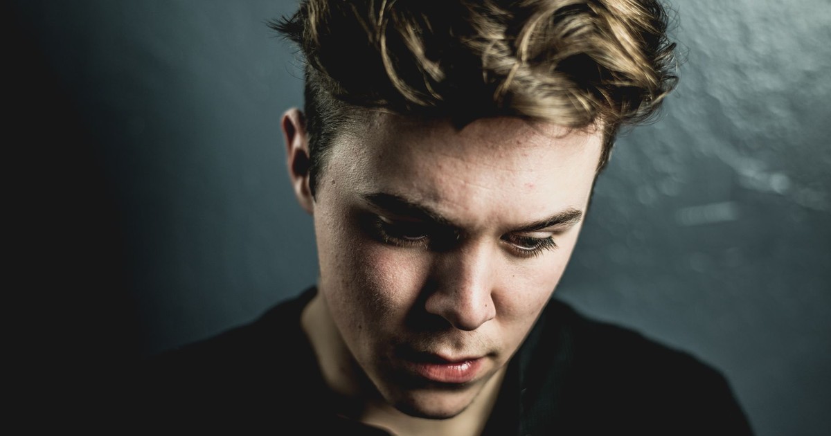 Close-up portrait of a young man with a thoughtful expression against a dark background.