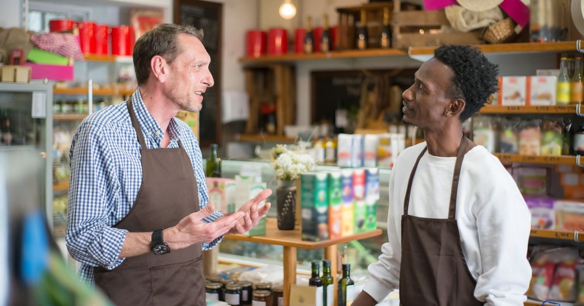 Two colleagues in aprons conversing in a grocery store setting.