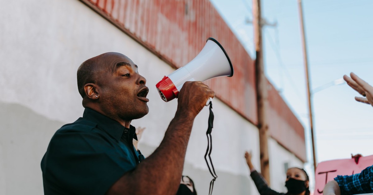 African American man using megaphone to lead a protest outdoors during the day.