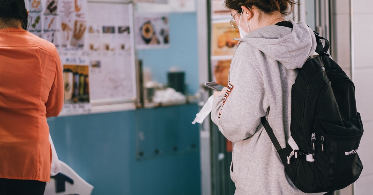 Young woman wearing mask and hoodie standing at a food stall in Sydney during the day.