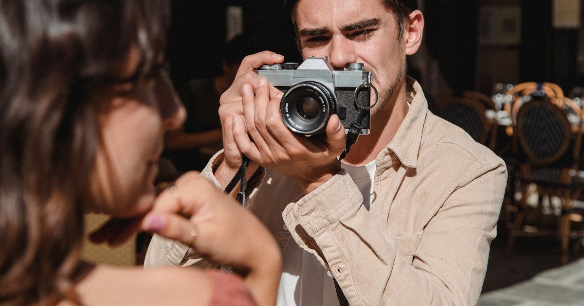 A man taking a photo of a woman with a vintage camera in an outdoor cafe setting.