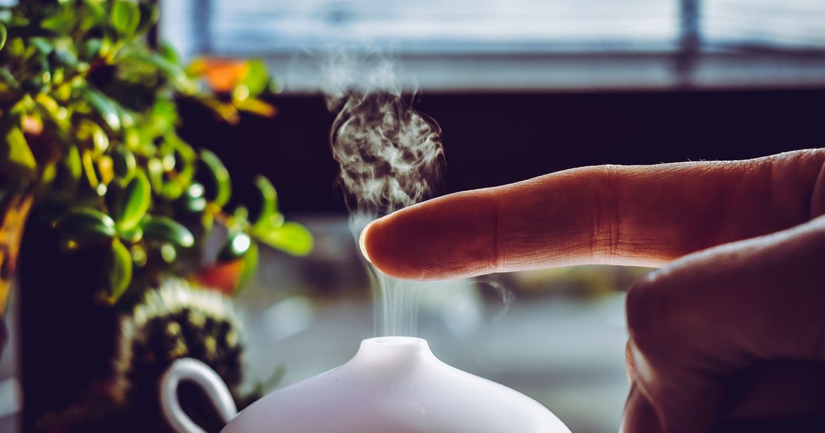 A hand touches mist rising from a diffuser, creating a relaxing ambiance indoors.