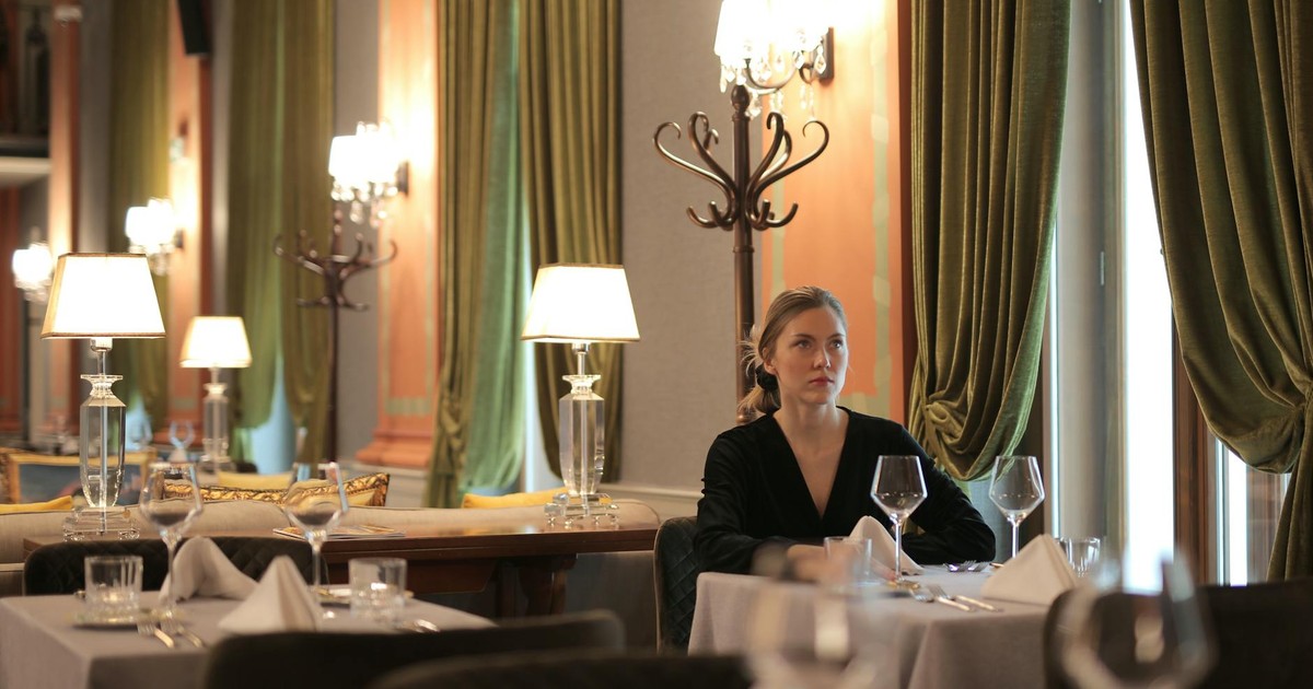 Woman sitting alone in a luxurious restaurant, surrounded by elegant decor and dim lighting.