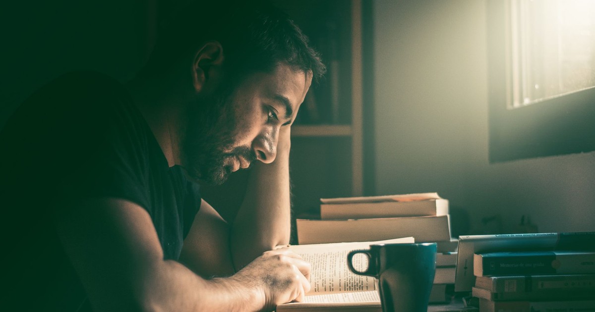 An adult man immersed in reading by the window in Madrid. Warm, focused study atmosphere.