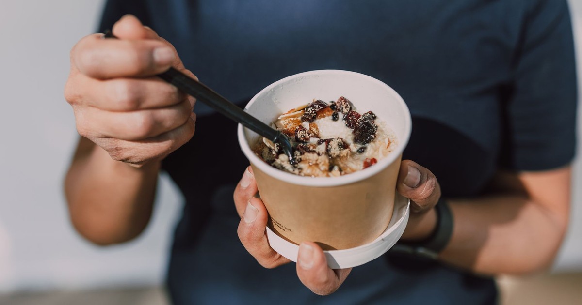 Hands holding a cup of vegan oatmeal with fruits and nuts, perfect for a healthy breakfast on the go.