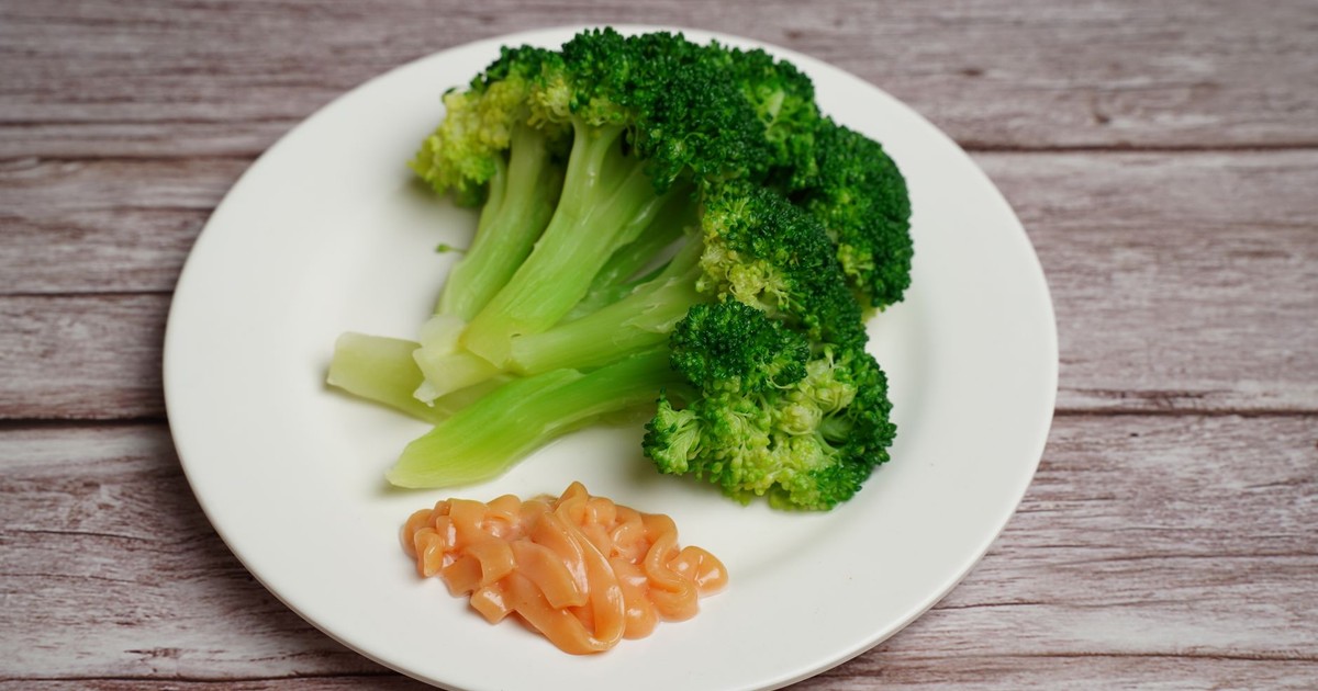 A close-up of fresh steamed broccoli served with sauce on a white plate, highlighting healthy cuisine.