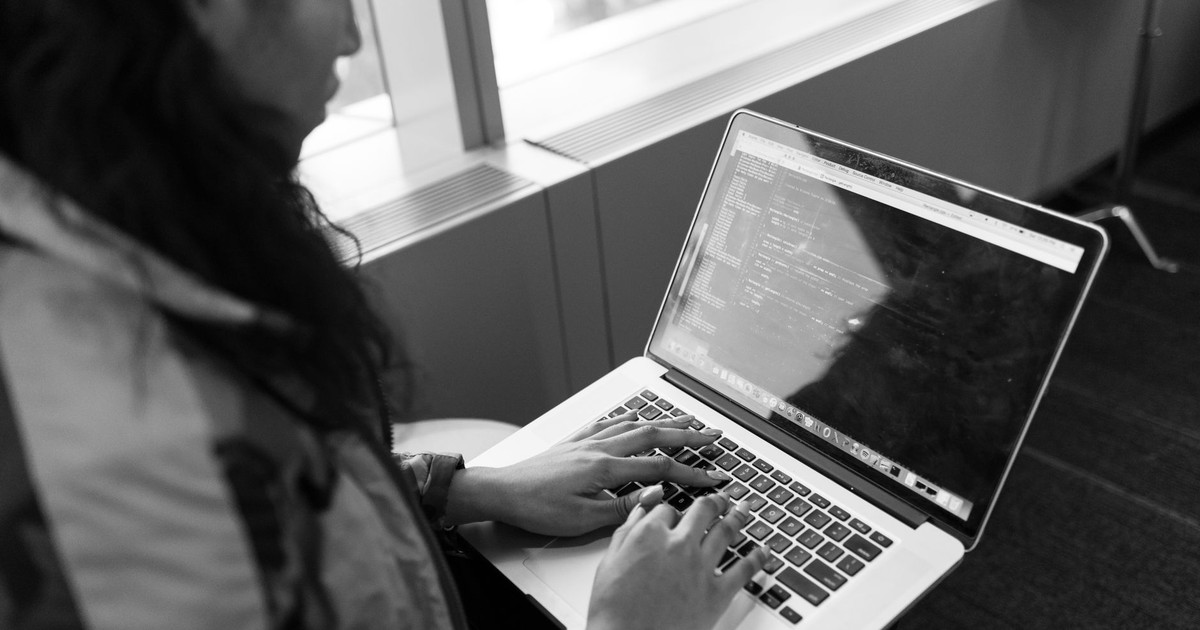A woman typing code on a laptop in a modern indoor setting, showcasing tech work.