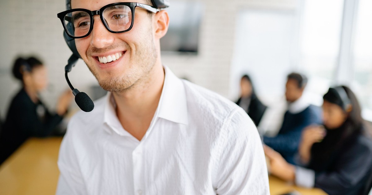 Friendly customer service representative wearing a headset, smiling in a busy office environment.