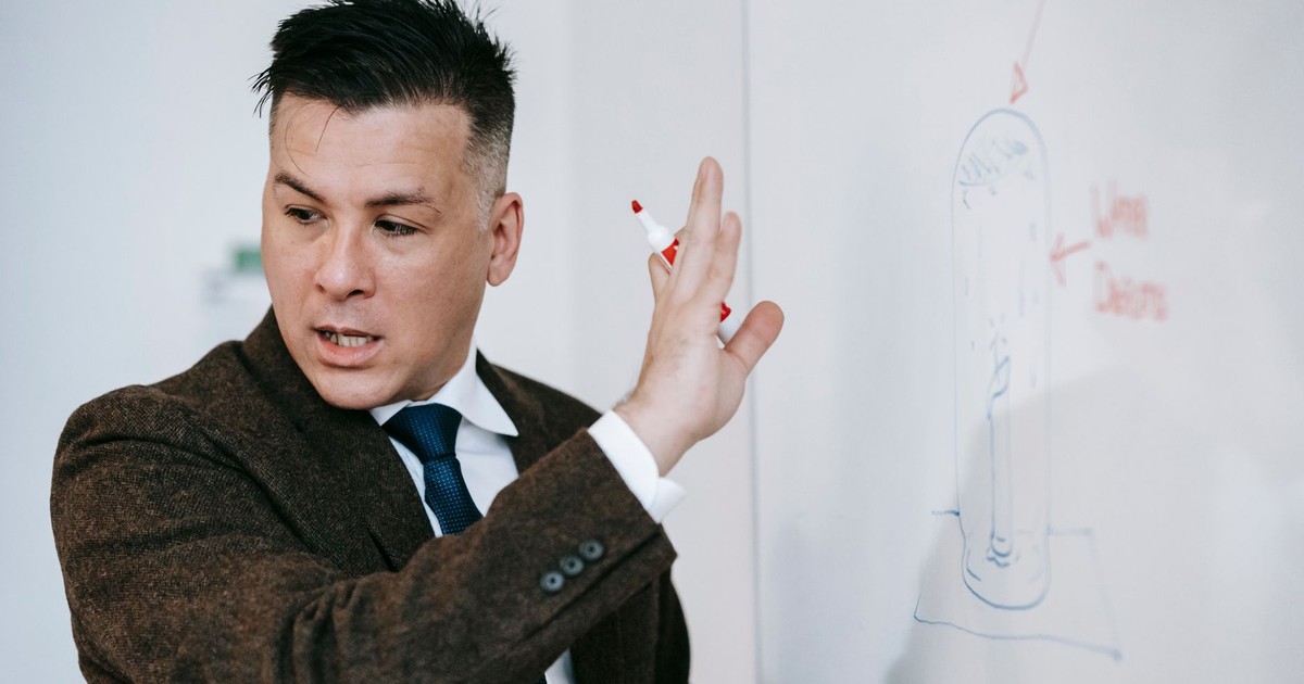Man in formal attire presenting ideas on a whiteboard in an educational setting.