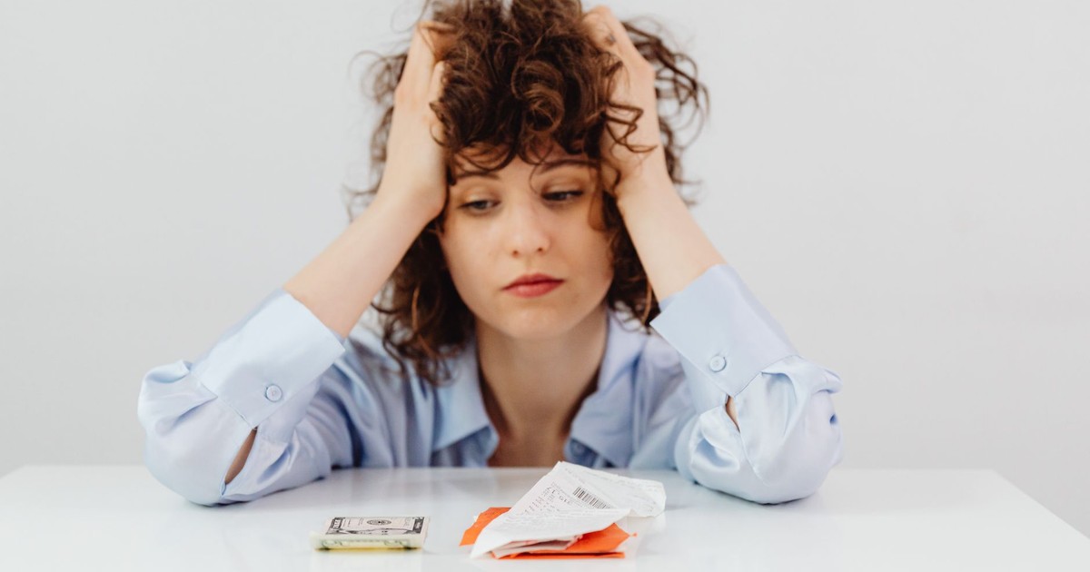 Woman in blue sleeves appears stressed while looking at receipts and money, symbolizing financial stress.