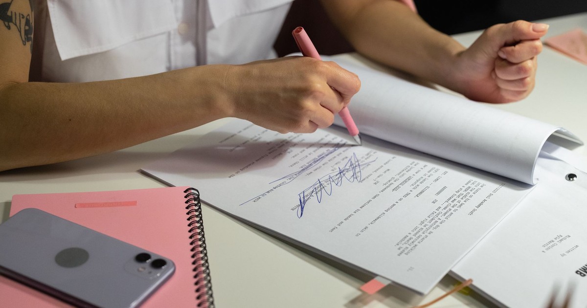 Close-up of a person writing on documents at a well-organized office desk.