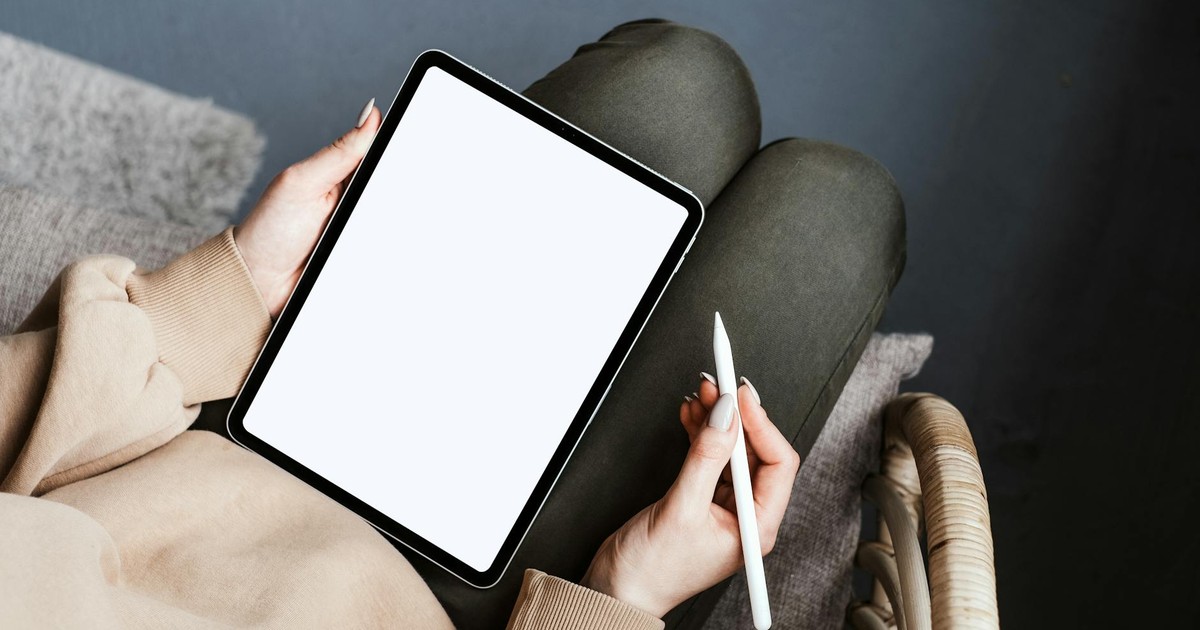 A person using a tablet with a stylus in a cozy, relaxed indoor setting on a chair.