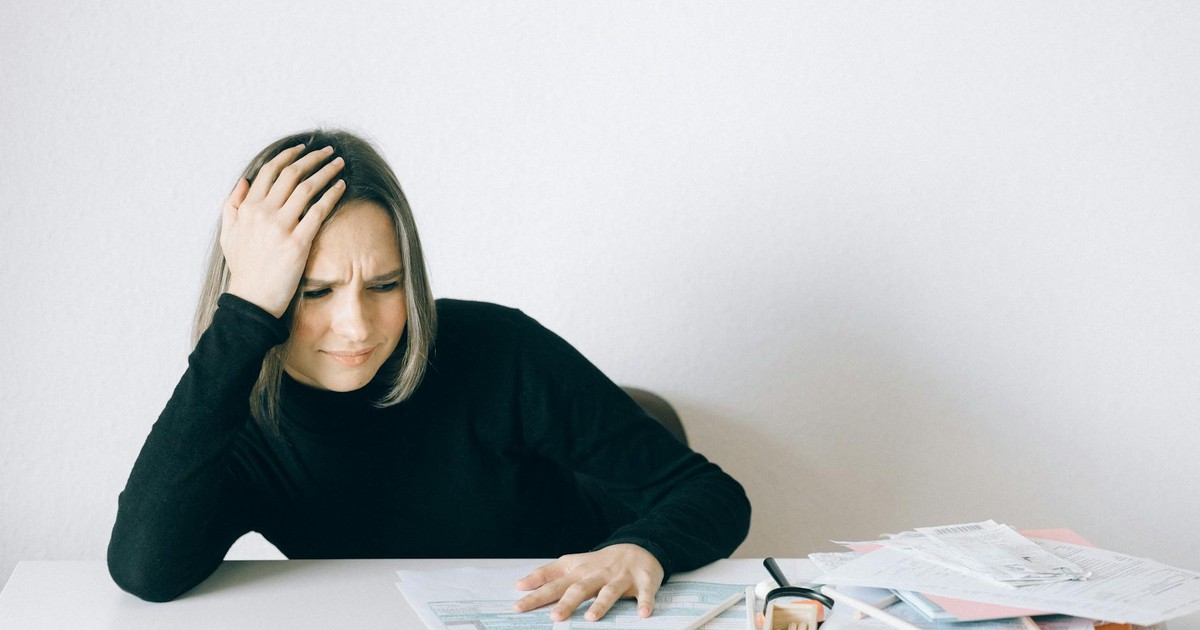 Woman in black sweater stressed with financial paperwork, overwhelmed at white table.