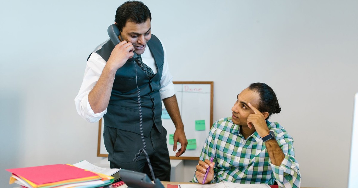 Two male colleagues collaborating in office, one talking on phone