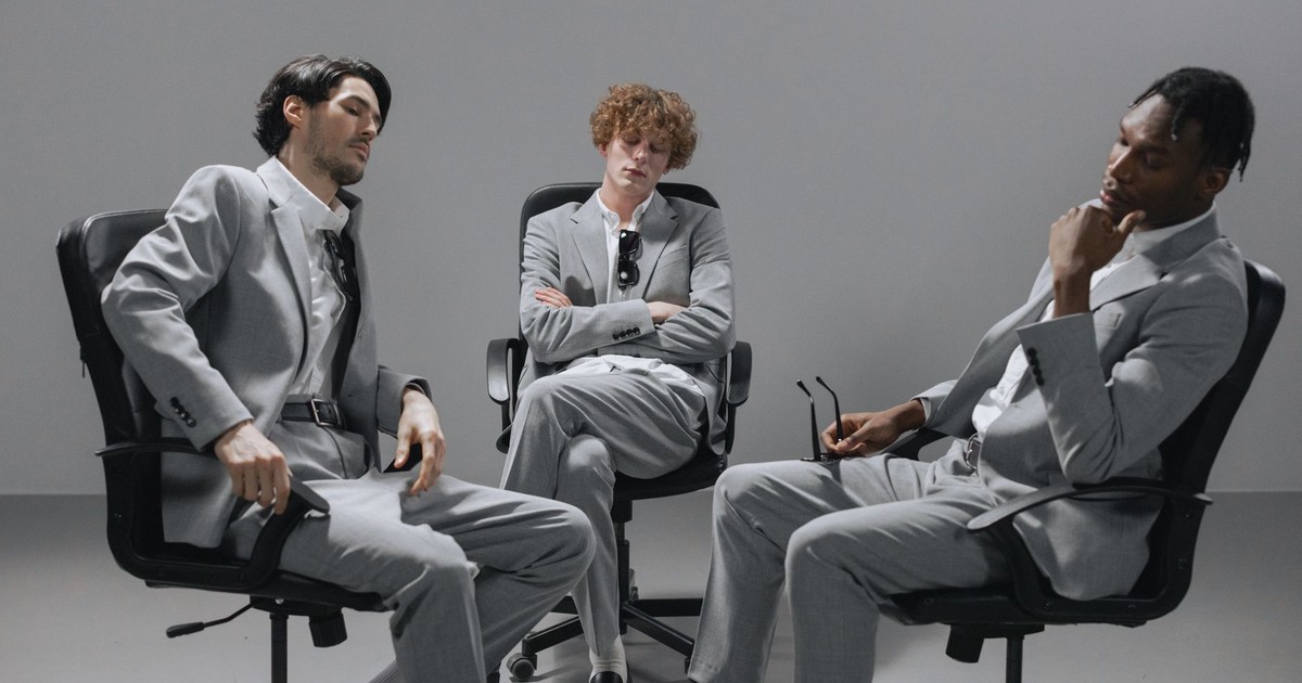 Three young professionals in gray suits collaborating in an office setting.
