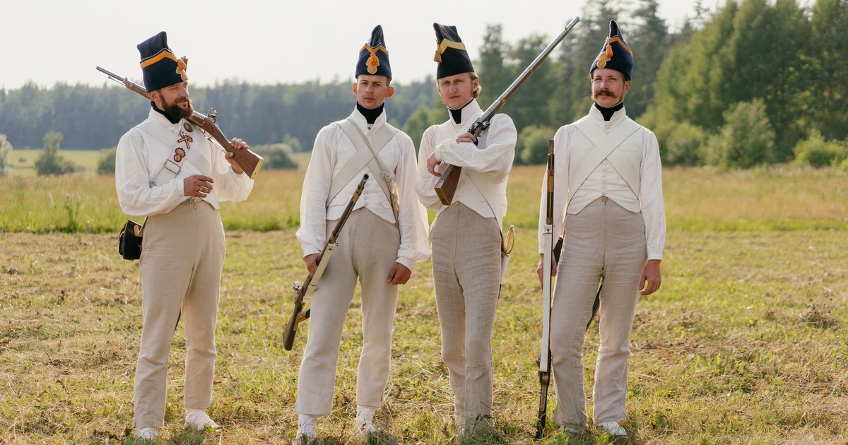 Four soldiers in vintage uniforms with rifles in a grassy field.