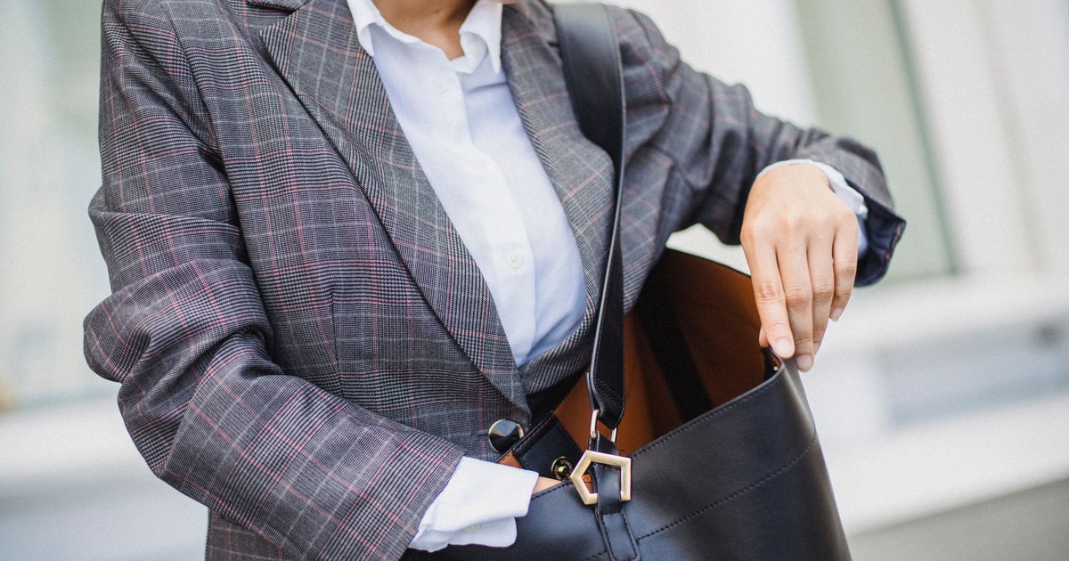 Close-up of a woman in a plaid blazer searching inside a leather bag outdoors.
