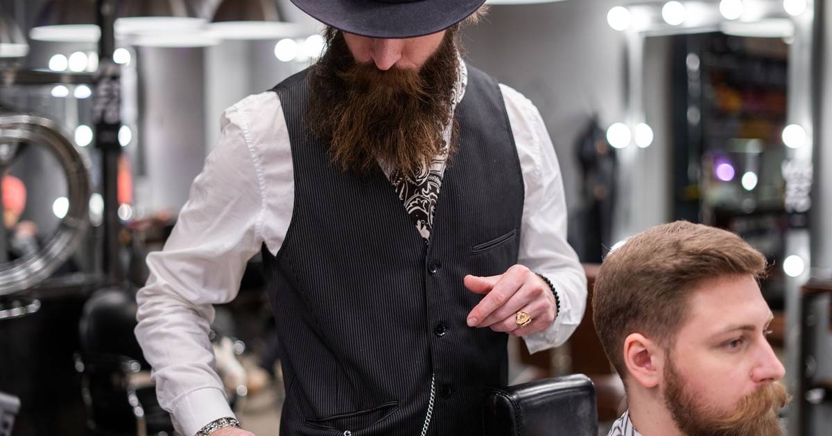 A bearded barber skillfully trims a client's hair in a modern barbershop setting.