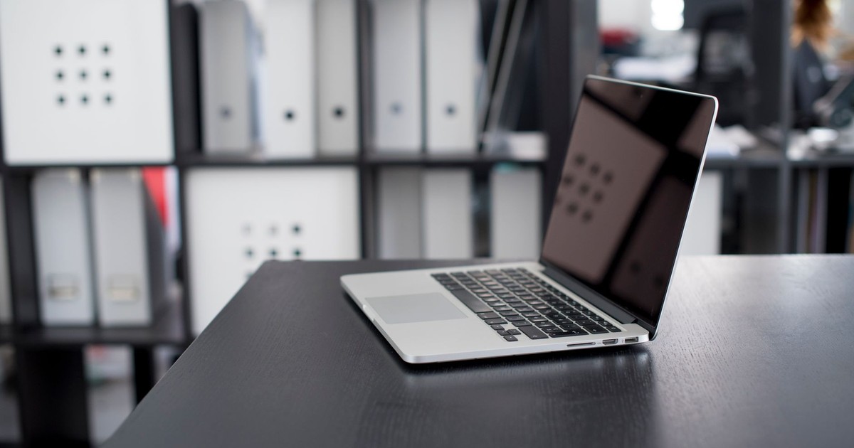 MacBook Pro displayed on a minimalist office desk with shelves in the background.