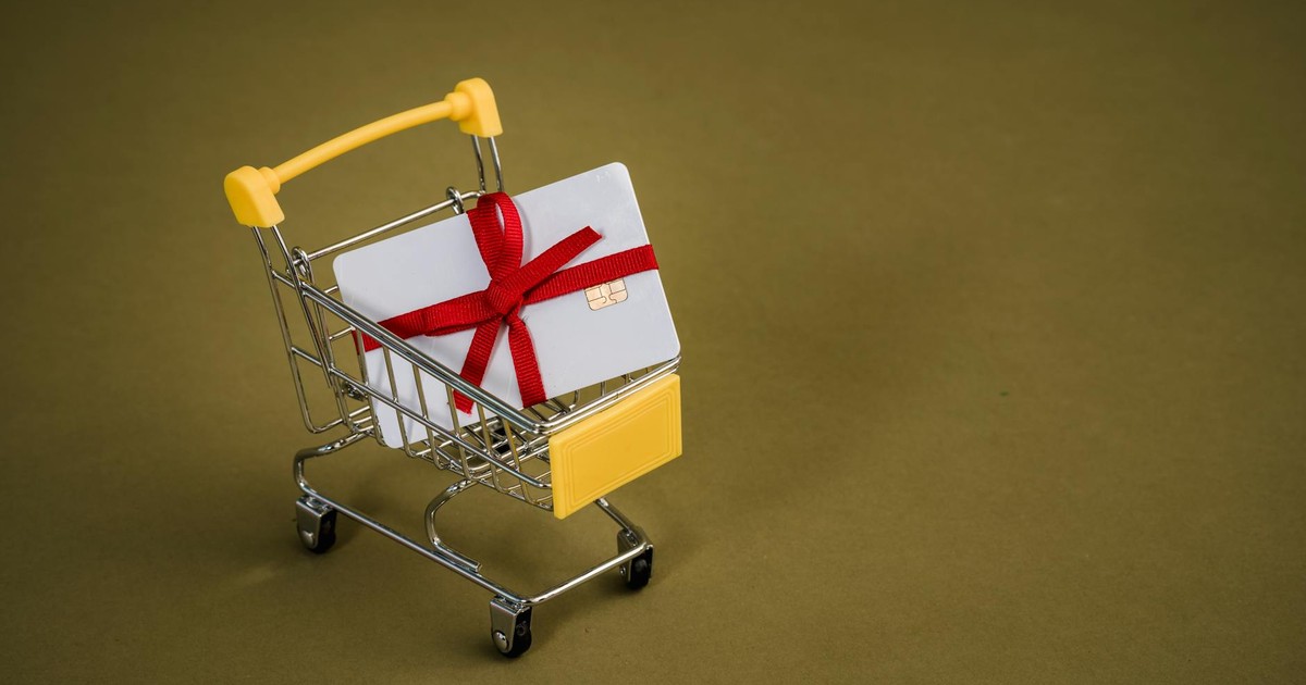 A gift card with a red bow sits in a mini shopping cart on a yellow backdrop.