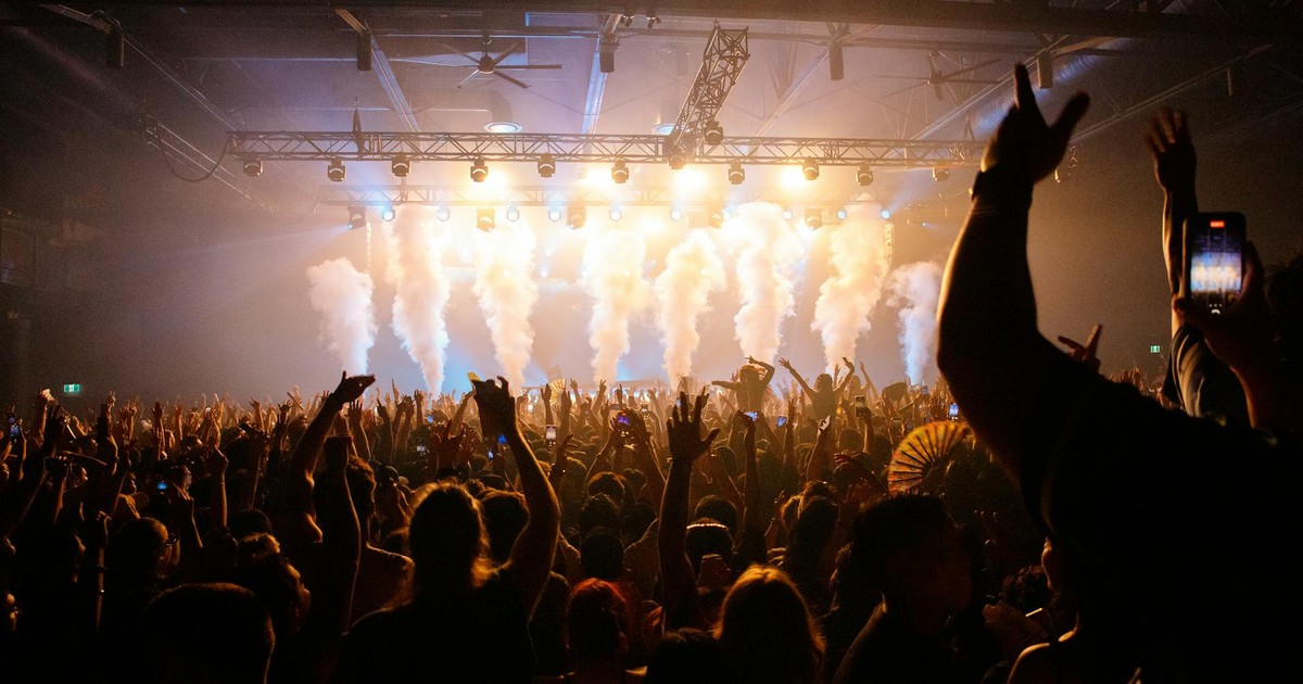 Energetic crowd enjoying a concert with dynamic lighting and smoke effects in an indoor venue.