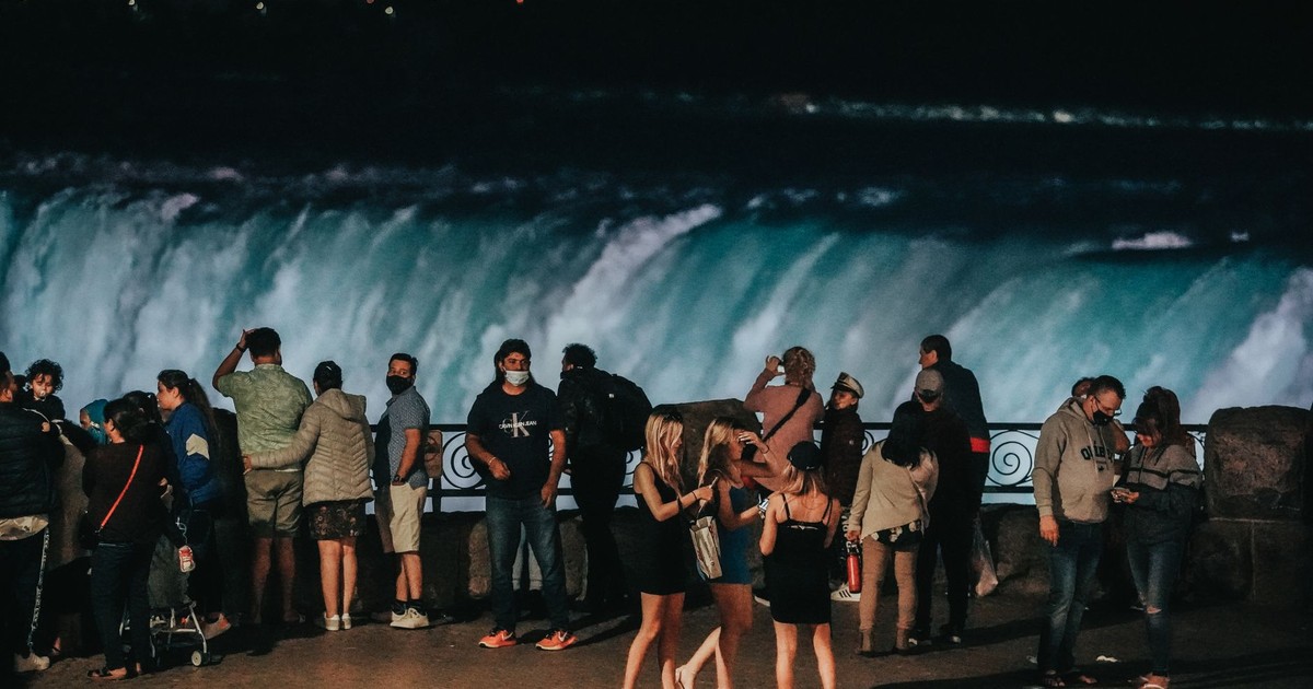 A group of tourists enjoying Niagara Falls at night with illuminated waters.