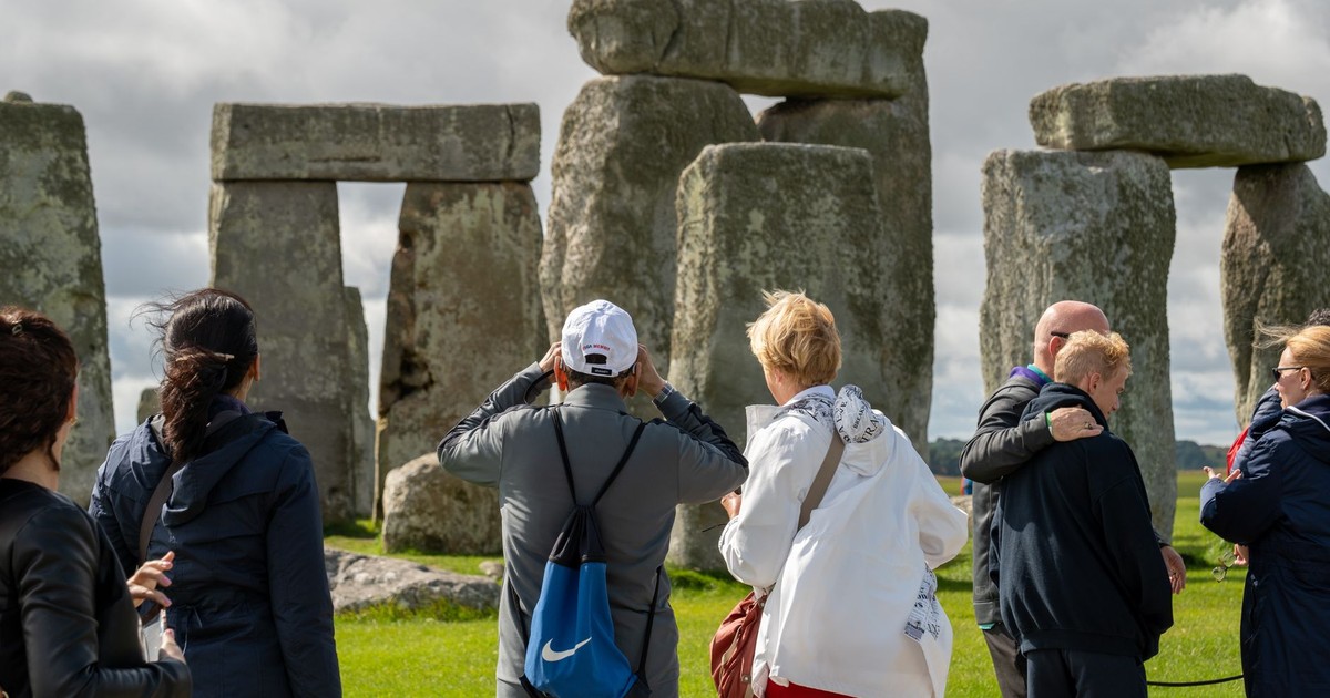 Visitors exploring the ancient Stonehenge monument under a cloudy sky, highlighting its historical significance.