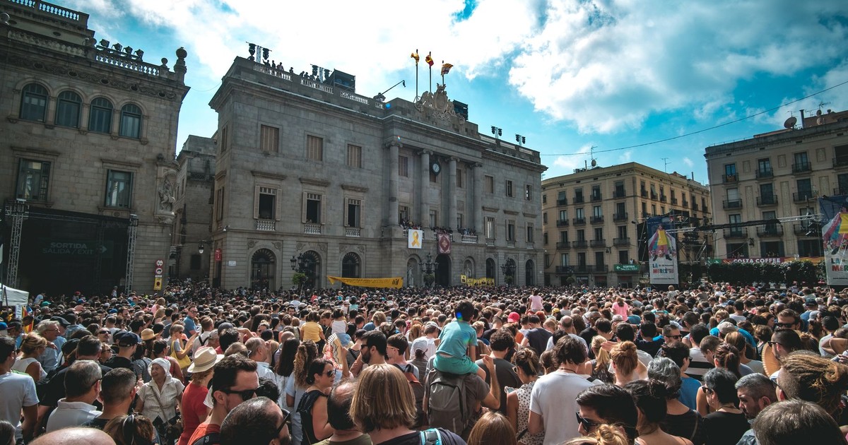 A lively gathering in a historic plaza in Barcelona, showcasing vibrant urban life under a bright sky.