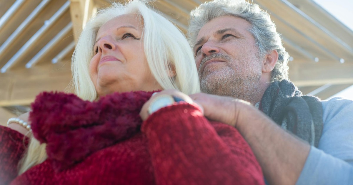 Loving senior couple embracing outdoors, under wooden structure in sunny Portugal.